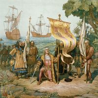 Christopher Columbus kneeling, holding flag and sword with two other men holding flags. There are other men on land and in boats behind Columbus and three ships in background. On the island named San Salvador by Columbus, later called Watling Island.