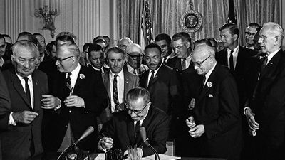 President Lyndon B. Johnson (Lyndon Johnson) signs the 1964 Civil Rights Act as Martin Luther King, Jr., others look on East Room, White House, Washington, D.C., July 2, 1964.