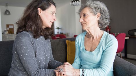 A photo of a serious elderly woman and her daughter talking and holding hands.