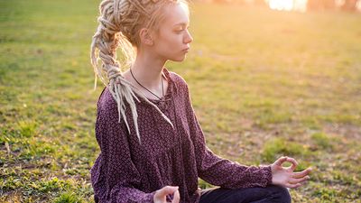 Young woman meditating in nature. About 20 years old, Caucasian female. dreadlocks